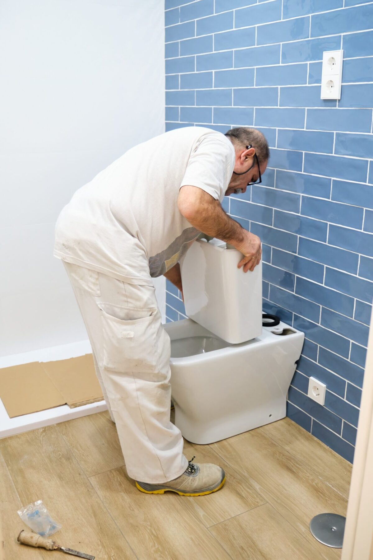 Senior plumber installer installing toilet cistern.